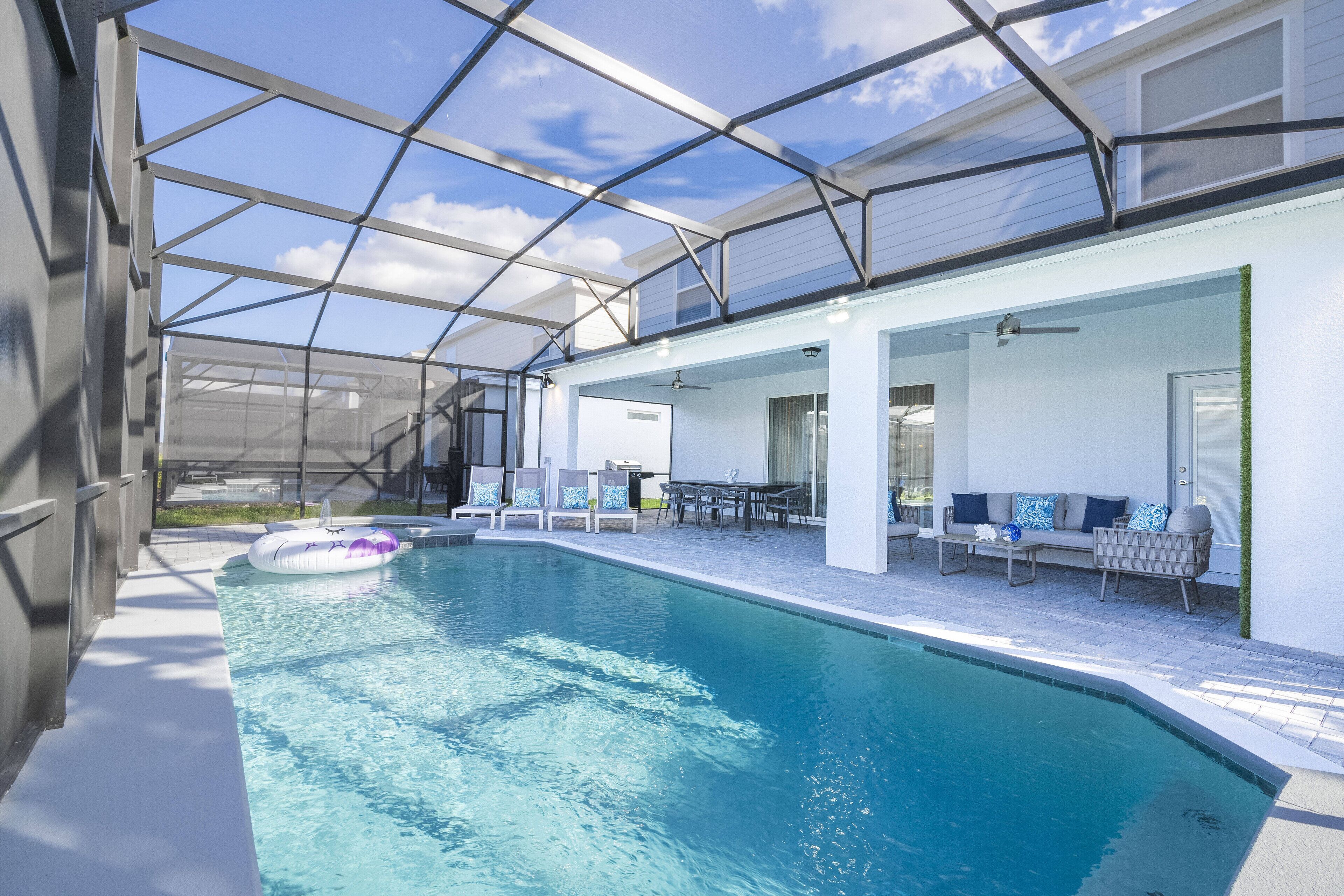 Ein Schwimmbecken mit Glasveranda, Sitzgelegenheiten im Freien und einem Deckenventilator.