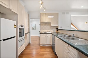 A modern kitchen with white cabinets, a stainless steel sink, and a wooden floor. - Spacious 4-bed House With Garden in Doncaster (Melbourne)