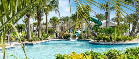 A pool area with a water slide, palm trees, and a clear blue sky.