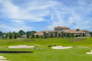 Un campo de golf con búnkeres de arena, una casa club y un edificio grande con tejado de azulejos.