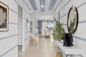 A modern hallway with a staircase, a dining area, and a wall-mounted mirror. - Last Minute Disney! Private Pool, Hot Tub, Game Room & Themed Bedrooms. Book Now! #WIR441 (Orlando)