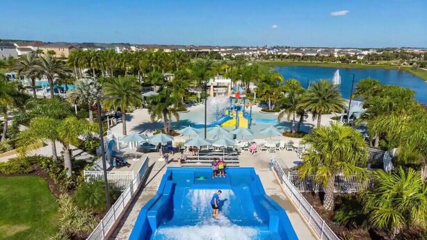 Un parque acuático con una piscina grande, palmeras y vistas del entorno.