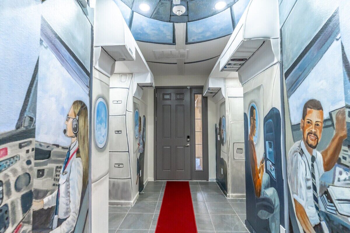 Un pasillo con alfombra roja que conduce a una puerta, flanqueado por paredes con murales alusivos al espacio.