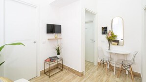 Moderni hotellihuone, jossa on taulutelevisio, pieni pöytä, jossa on kasvi, ja peili seinällä.
