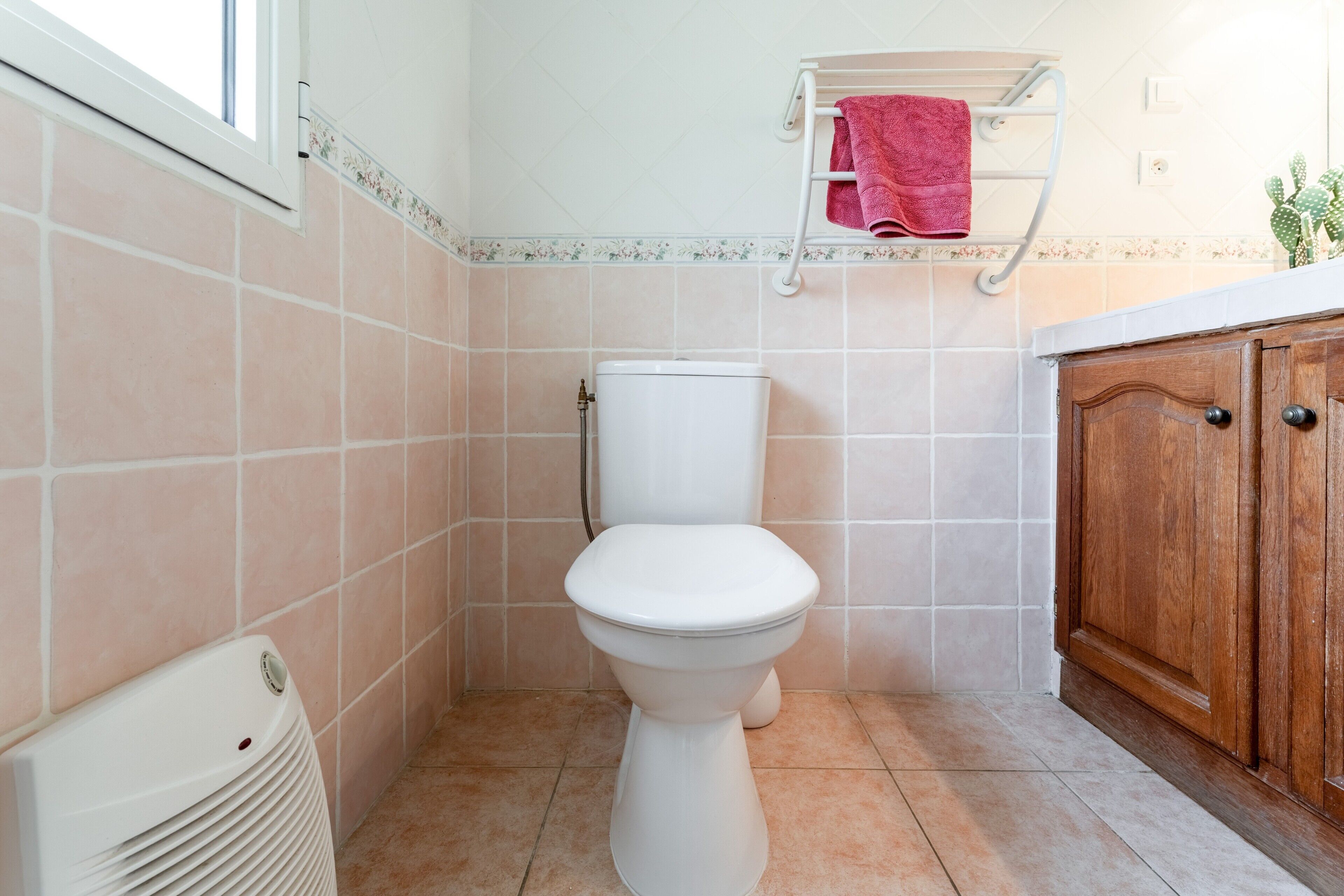 Un baño con inodoro, un radiador blanco, un armario de madera y un perchero con una toalla roja.