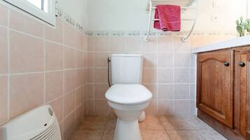Un baño con inodoro, un radiador blanco, un armario de madera y un perchero con una toalla roja.