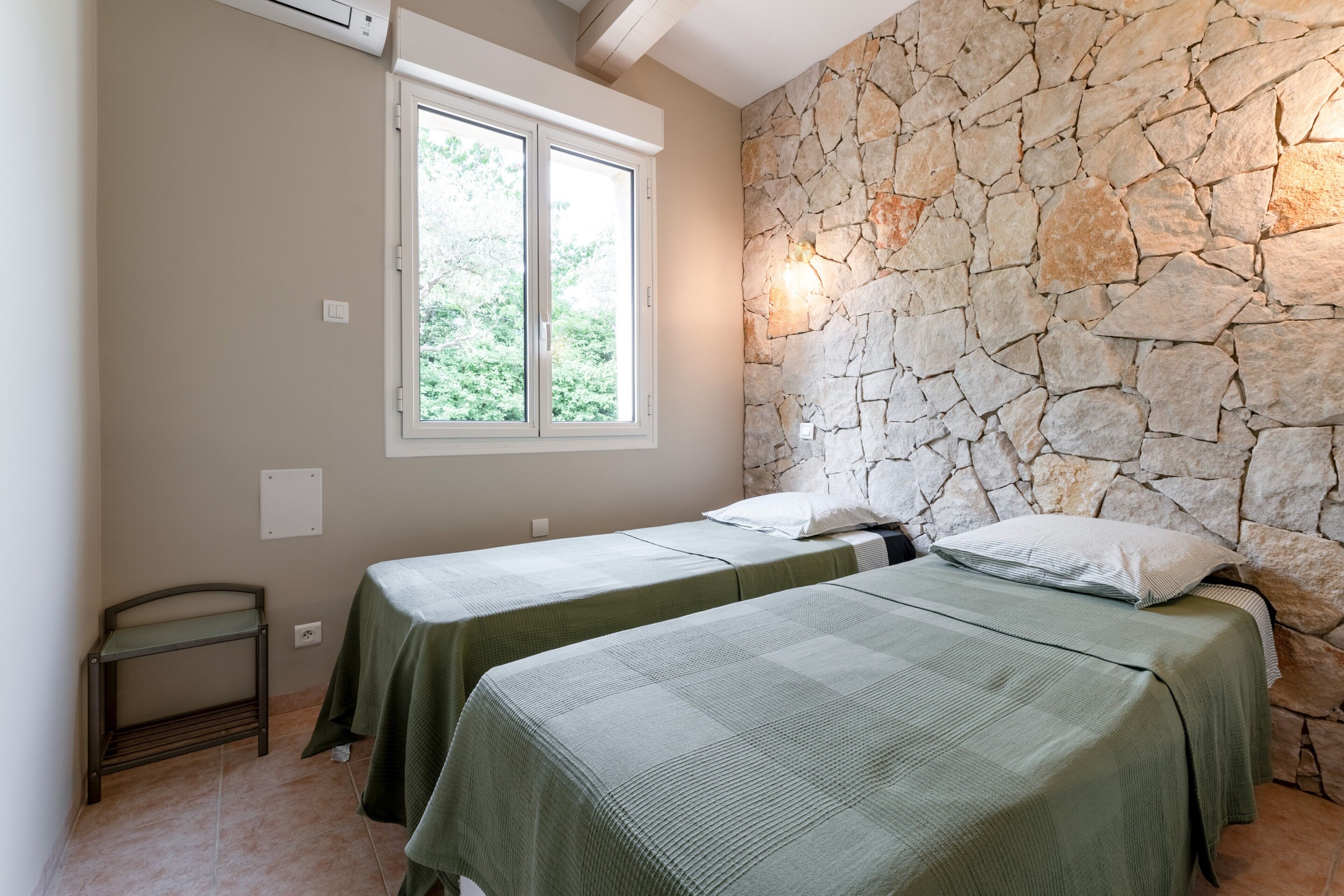 Une chambre avec deux lits, un mur en pierre, une fenêtre et une petite table.