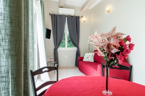 Una habitación con una mesa roja, un jarrón con flores, un sofá rojo y una ventana con cortinas.