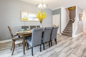 A dining area with a wooden table, grey upholstered chairs, a vase with yellow flowers, and a chandelier. - Disney Getaway! Luxury Villa with Private Pool & Game Room. Book Now! #CG886 (Orlando)