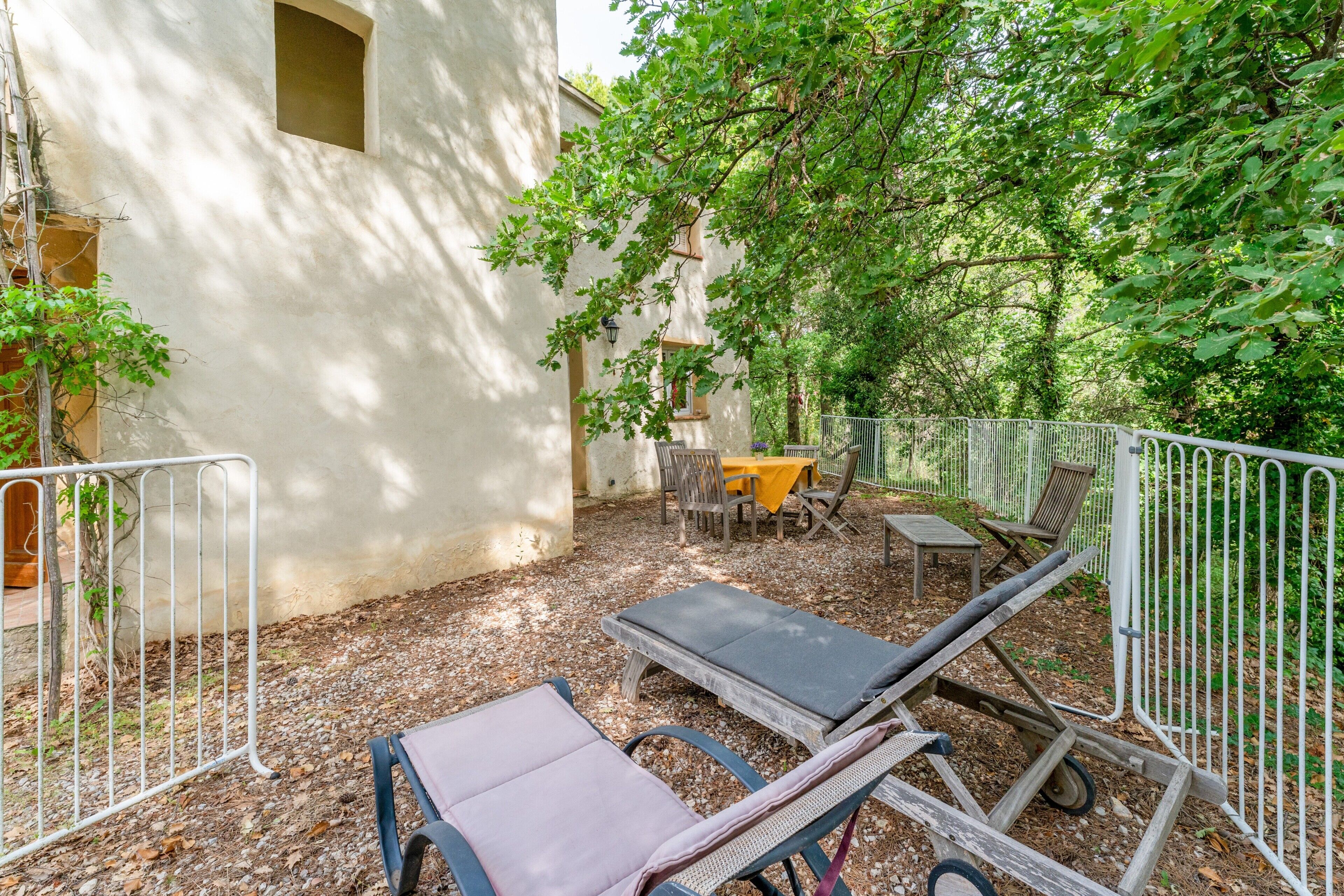 A courtyard with a table and chairs, a lounge chair, and a small table with a yellow tablecloth.