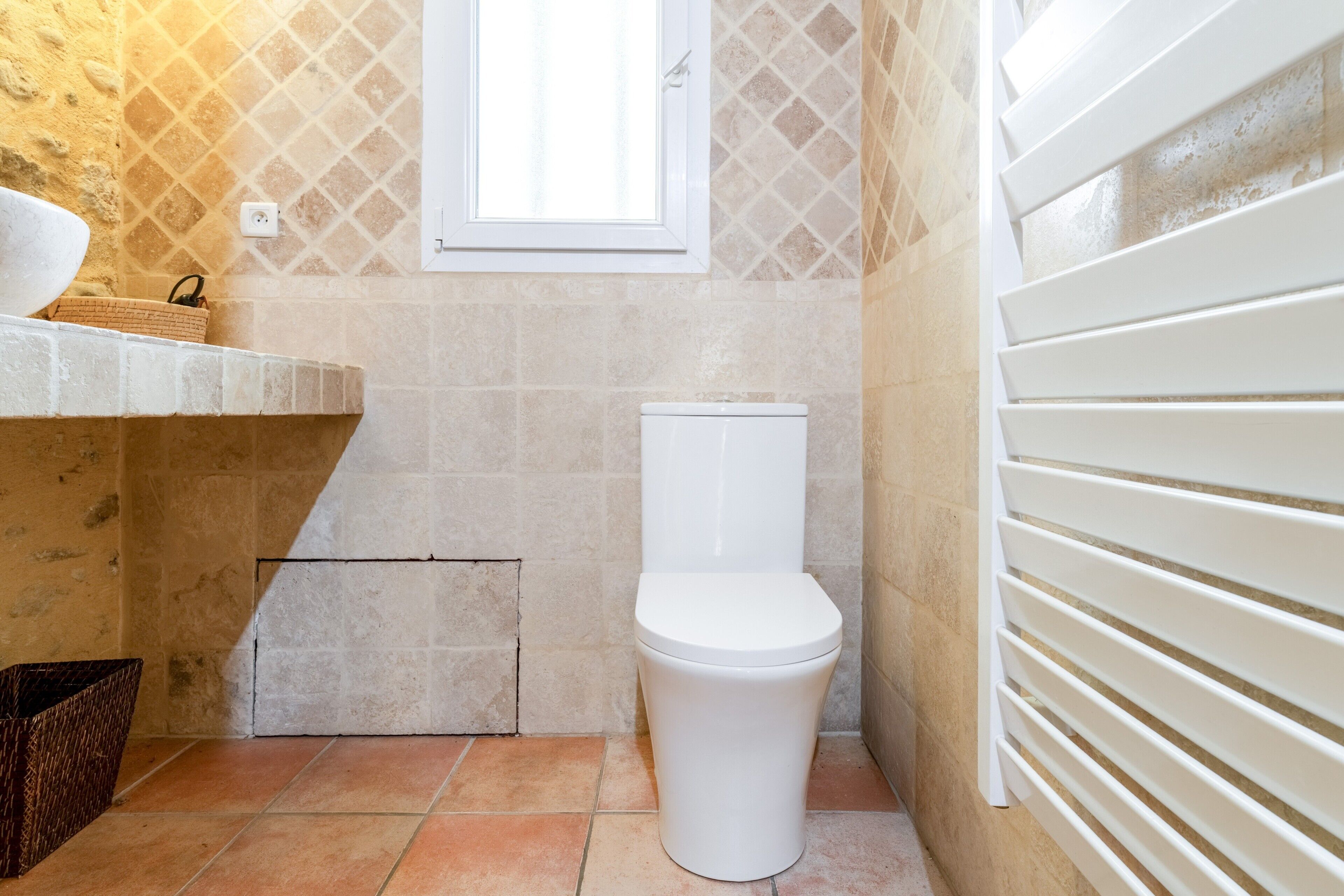 A bathroom with a white toilet, a window, and a tiled wall.