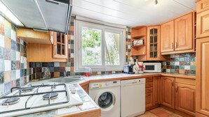 A kitchen with a gas stove, washing machine, microwave, and wooden cabinets.