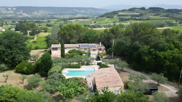 A villa with a swimming pool, surrounded by lush greenery and a scenic countryside view.