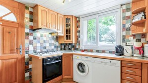 A compact kitchen with wooden cabinets, a built-in oven, a dishwasher, and a window overlooking greenery.