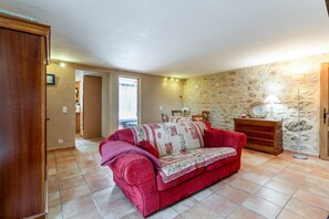 A red sofa in a room with stone walls, a wooden cabinet, and a lamp. - Apartment 'Gite Du Petit Bois - Bignone' with Shared Pool, Wi-Fi and Air Conditioning (Villedieu)