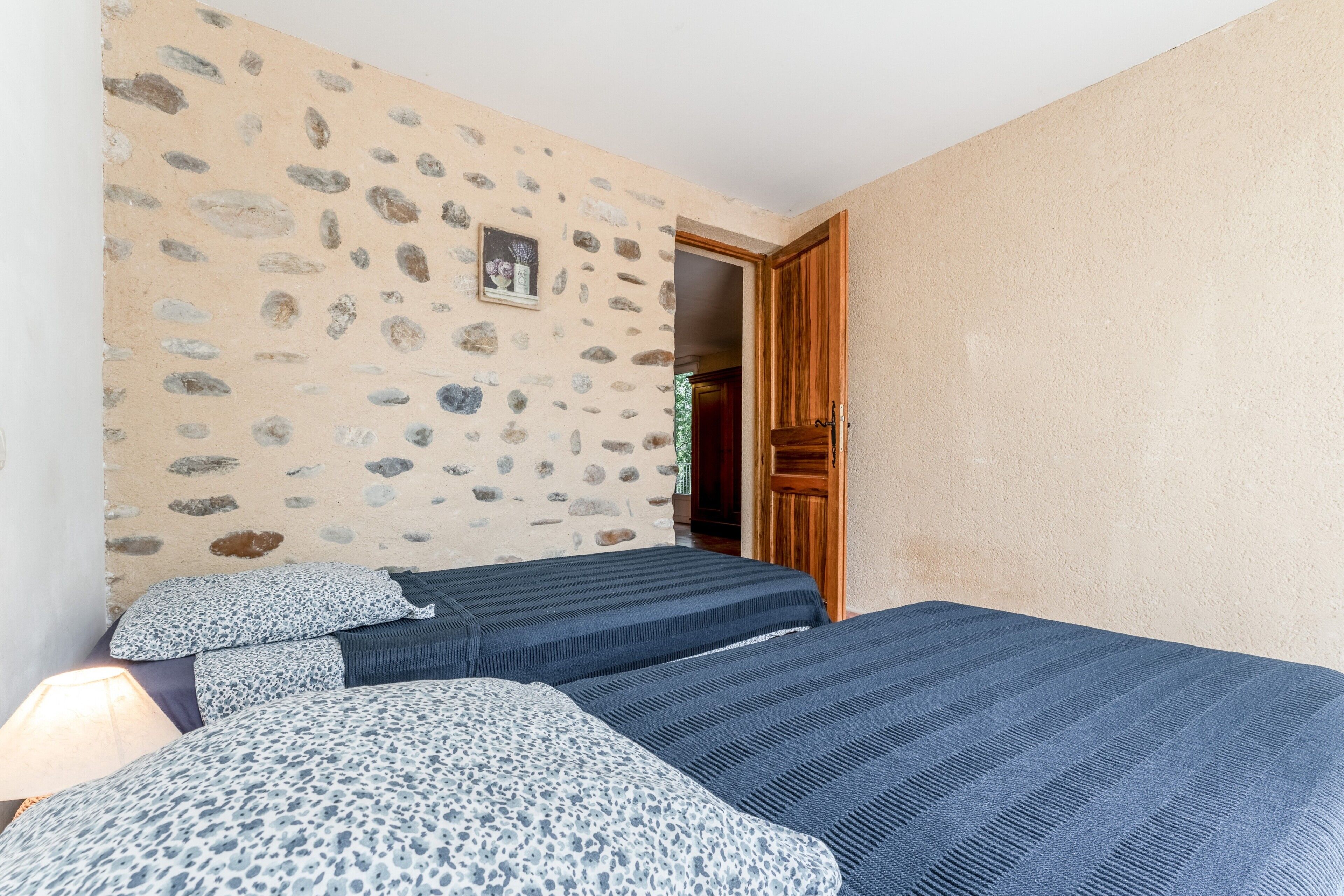 Une chambre avec deux lits, un mur en pierre et une porte en bois.