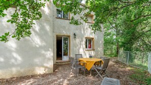 A rustic outdoor seating area with a table and chairs, a gravel ground, and a building with a door and windows.