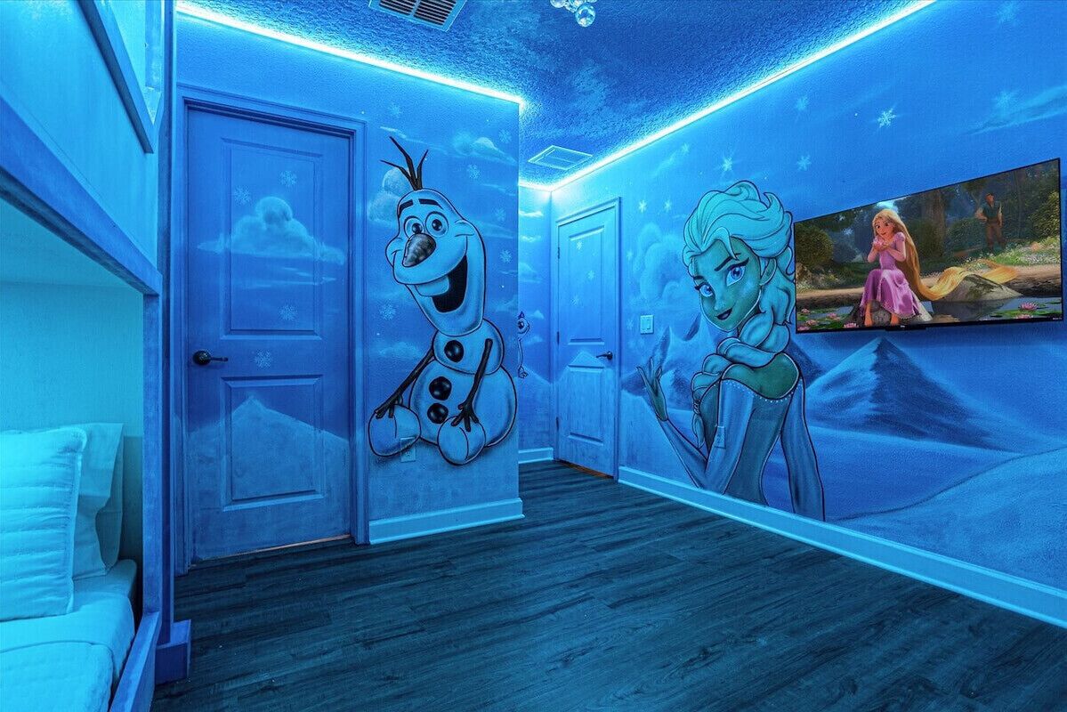 A room with a blue-themed mural, a bed, and a television screen displaying a movie scene.