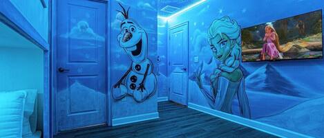 A room with a blue-themed mural, a bed, and a television screen displaying a movie scene.