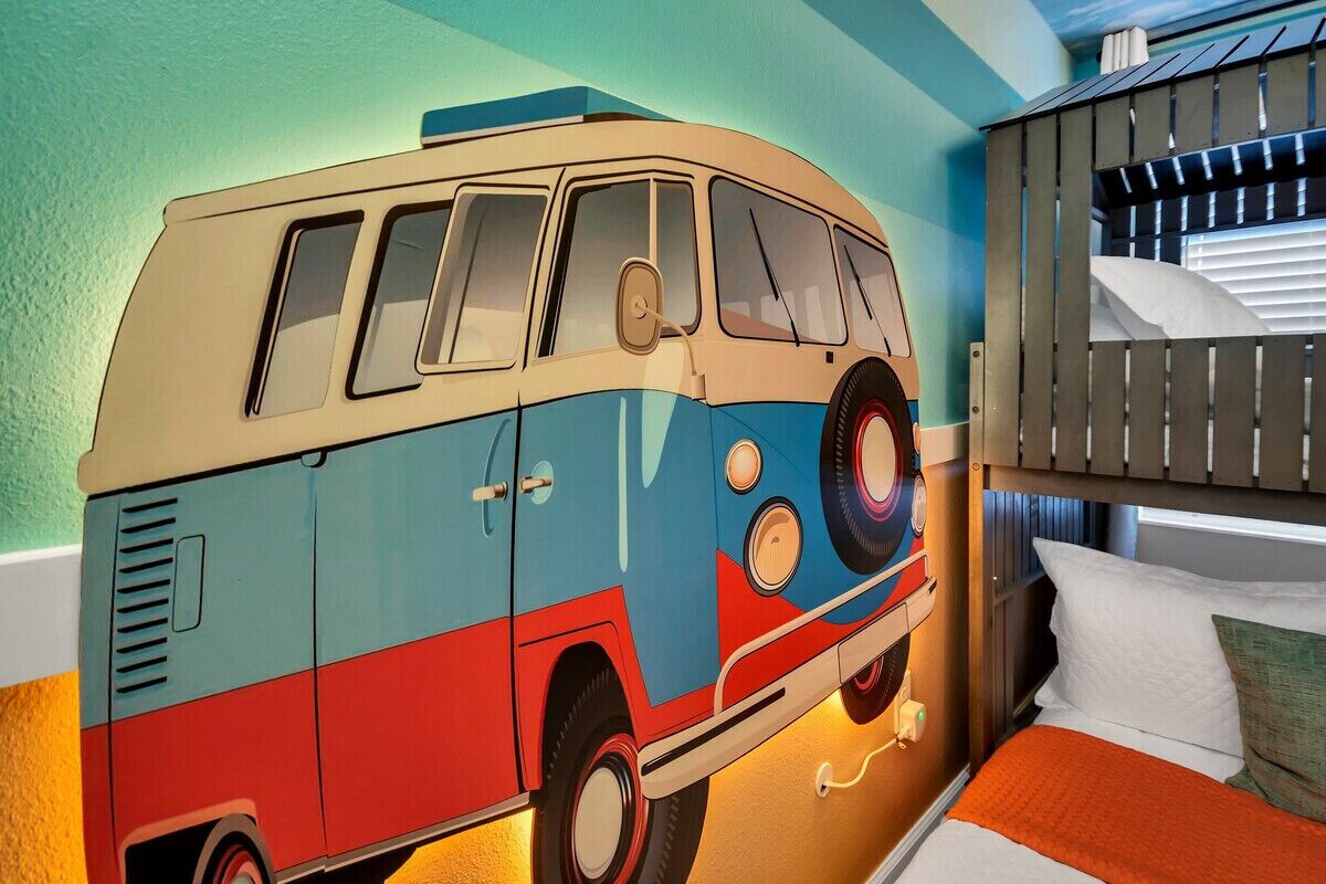 Una habitación con un mural de una furgoneta, camas literas y una cama con una manta naranja.