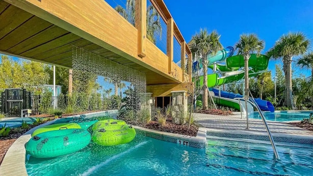 A pool area with two green inflatable tubes, a water slide, and a covered deck. - Last Minute Disney! Private Pool, Hot Tub, Game Room & Themed Bedrooms. Book Now! #WIR437 (Orlando)