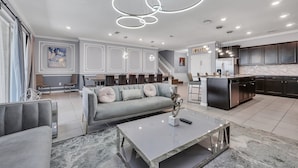 A modern living room with a grey sofa, a marble coffee table, and a staircase leading to a kitchen area. - Last Minute Disney! Private Pool, Hot Tub, Game Room & Themed Bedrooms. Book Now! #WIR437 (Orlando)