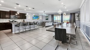 A modern kitchen with dark cabinets, a large island, and a dining area with a long table and chairs. - Last Minute Disney! Private Pool, Hot Tub, Game Room & Themed Bedrooms. Book Now! #WIR437 (Orlando)