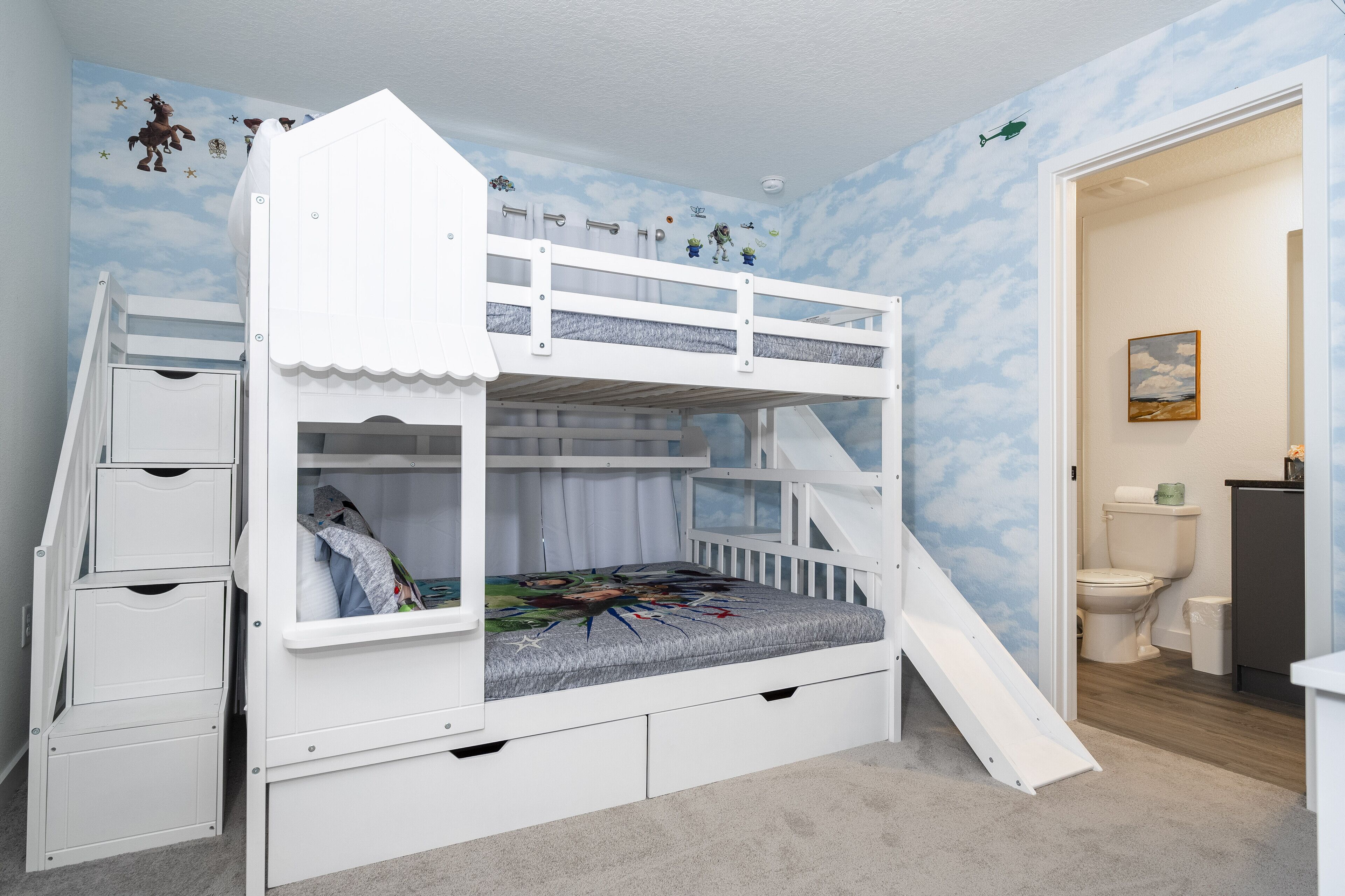 Un lit superposé avec un toboggan, un petit bureau et un placard.
