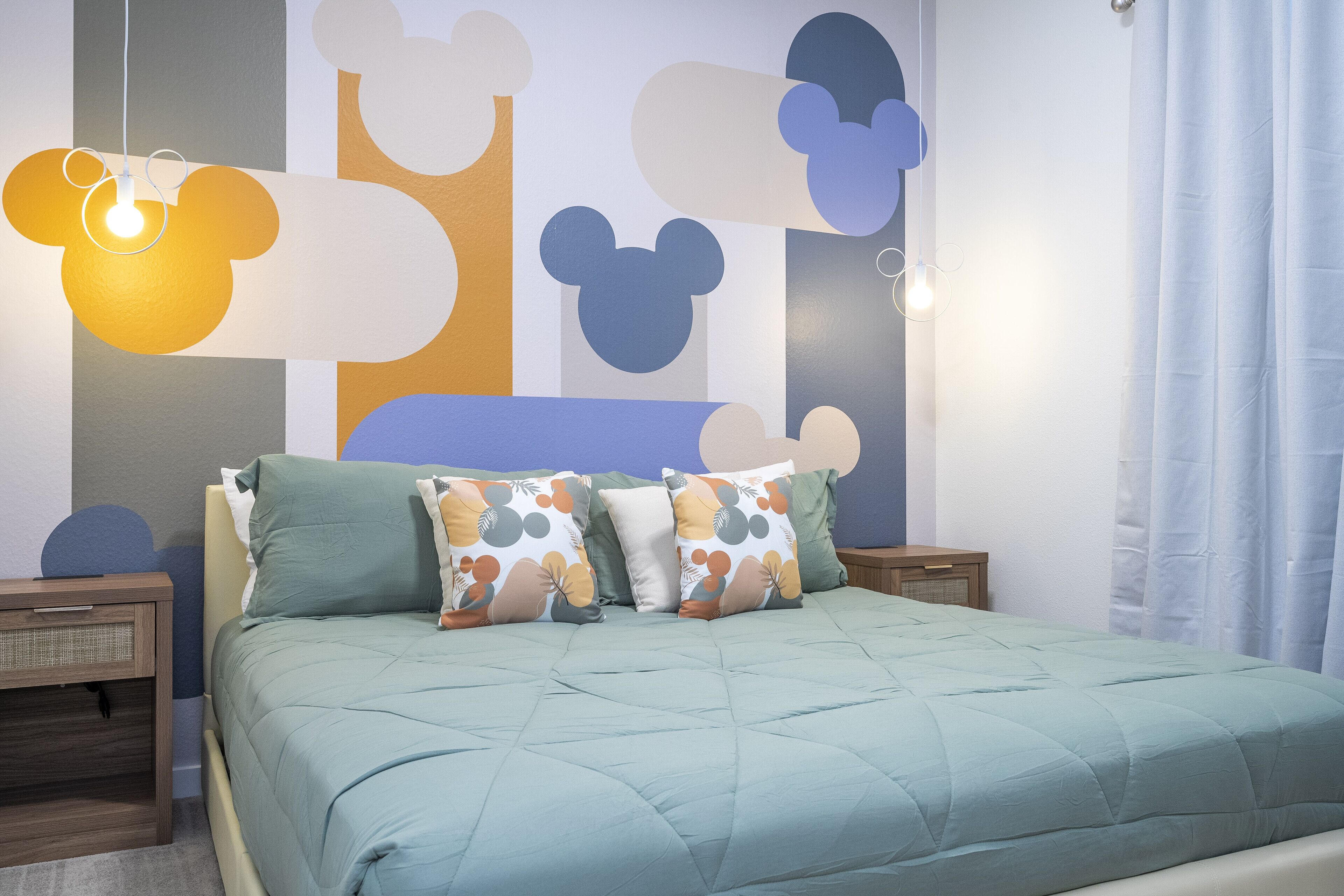 Un letto con una coperta azzurra, due comodini e una parete con forme astratte.