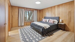 A bedroom with a bed, nightstand, and window with curtains. - Private Lake Simcoe Retreat | Sandy Beach, Sunsets, Kayaks & Ice Fishing (Beaverton)