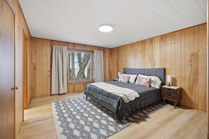 A bedroom with a bed, nightstand, and window with curtains. - Private Lake Simcoe Retreat | Sandy Beach, Sunsets, Kayaks & Ice Fishing (Beaverton)