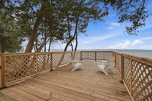 A wooden deck with a lattice railing, overlooking a body of water. - Private Lake Simcoe Retreat | Sandy Beach, Sunsets, Kayaks & Ice Fishing (Beaverton)