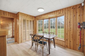 Une pièce aux murs lambrés, avec une table et des chaises, de grandes fenêtres et un luminaire au plafond.