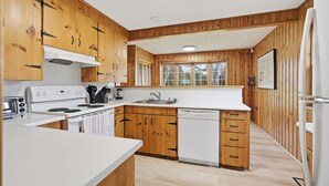 A compact kitchen with wooden cabinets, a white countertop, a built-in oven, a dishwasher, and a window above the sink. - Private Lake Simcoe Retreat | Sandy Beach, Sunsets, Kayaks & Ice Fishing (Beaverton)