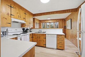 A compact kitchen with wooden cabinets, a white countertop, a built-in oven, a dishwasher, and a window above the sink. - Private Lake Simcoe Retreat | Sandy Beach, Sunsets, Kayaks & Ice Fishing (Beaverton)