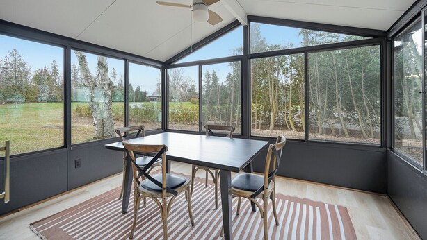 A conservatory with a table and chairs, large windows, and a ceiling fan. - Private Lake Simcoe Retreat | Sandy Beach, Sunsets, Kayaks & Ice Fishing (Beaverton)