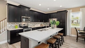 A modern kitchen with dark cabinets, a white island, and a large window with curtains. - Last Minute Disney Getaway! Townhouse with Private Pool. Book Now! #136377 (Orlando)