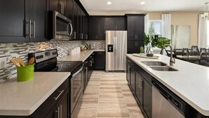 A modern kitchen with dark cabinetry, stainless steel appliances, a tiled backsplash, and a central island with a sink. - Last Minute Disney Getaway! Townhouse with Private Pool. Book Now! #136377 (Orlando)