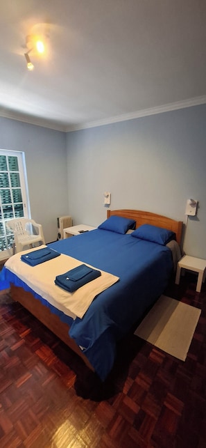 A neatly made bed with blue bedding, a wooden headboard, a white bedside table, and a small white stool. - Villa Meco Beach & Pool Private Pool Private Gym Your getaway in Meco (Setúbal)