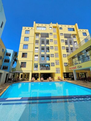A multi-story hotel with a swimming pool, balconies, and a sign reading 'THE HOME Plate'. - Zuri Premium Nyali, Furnished 1 Bedroom (Mombasa)