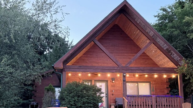A wooden cabin with a porch, picnic tables, and a barbecue grill.