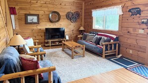 A cozy cabin interior with a wooden interior, a television, a sofa, and a dining table.