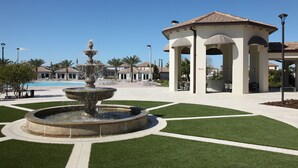Ein Springbrunnen mit mehreren Stufen, ein Kiosk und ein Pool in einer angelegten Grünfläche mit Wegen und Bepflanzung.