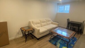 Een woonkamer met een beige bank, een glazen salontafel en een eettafel met stoelen.