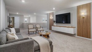 Un salon moderne avec un canapé gris, des fauteuils à rayures, une table basse et un téléviseur fixé sur un mur recouvert de panneaux en bois.