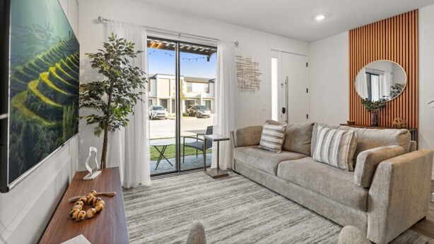 A modern living room with a sofa, a coffee table, and a large painting. There is a sliding glass door leading to an outdoor area. - Last Minute Disney Getaway! Modern Townhome. Book Now! #158993 (Orlando)