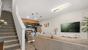A modern living room with a staircase, a kitchen area, and a large flat-screen TV on the wall. - Last Minute Disney Getaway! Modern Townhome. Book Now! #158993 (Orlando)
