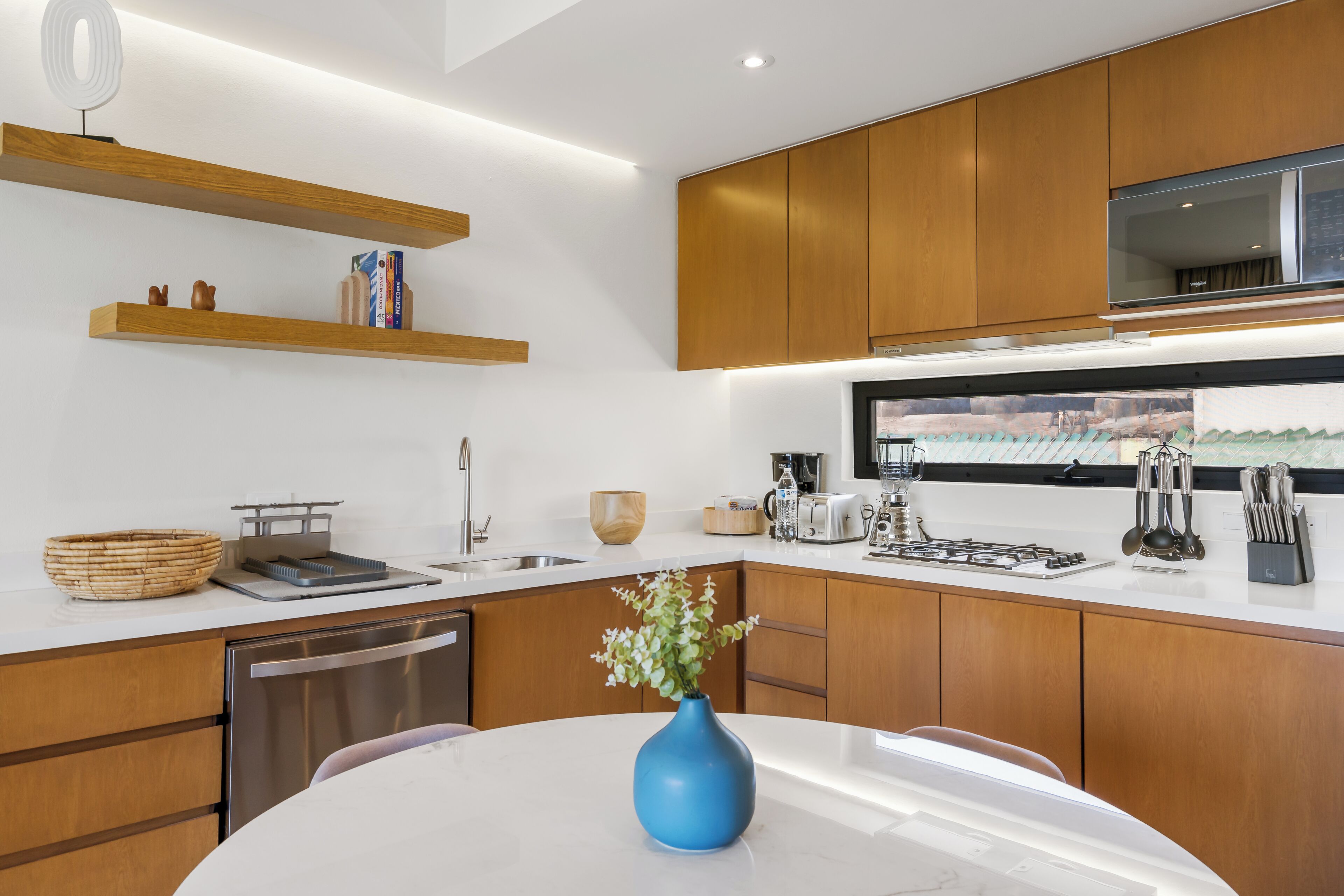 Uma cozinha moderna com armários de madeira, bancada branca, vaso azul e eletrodomésticos de aço inoxidável.