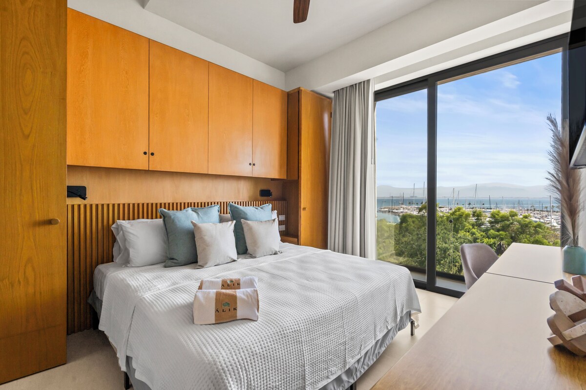 Ein modernes Schlafzimmer mit einem großen Bett, Holzschränken, Blick auf die Stadt und einem Essbereich.