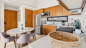 A modern kitchen with wooden cabinets, a stainless steel refrigerator, a round dining table with chairs, and a large woven basket. - Alik (La Cruz de Huanacaxtle)